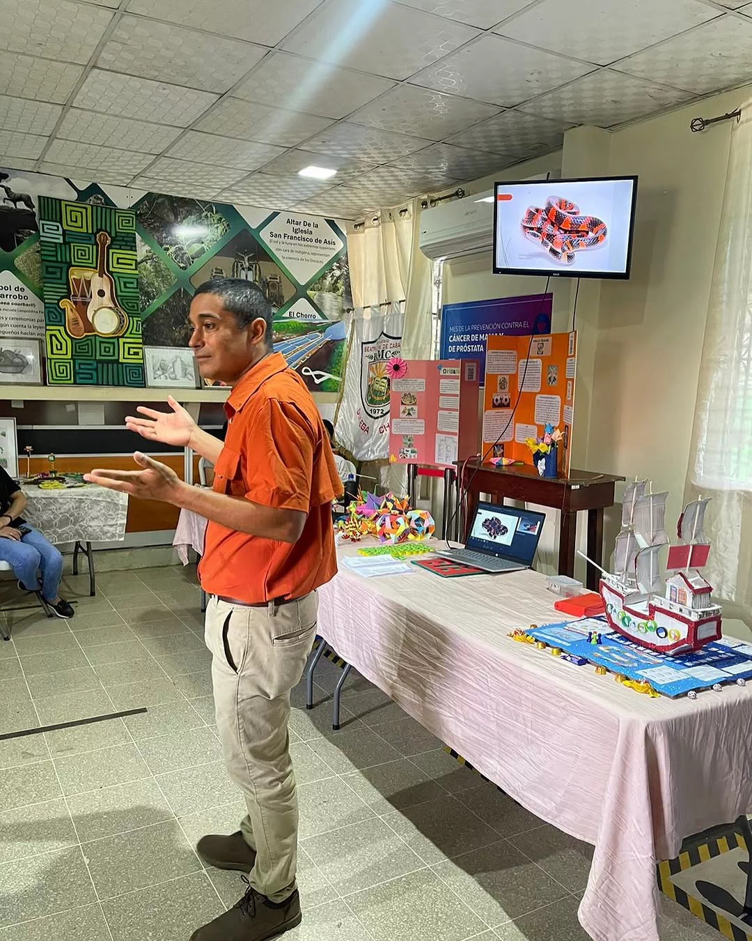 Miembro de la fundación presentando en una feria de ciencia escolar, con maquetas y una serpiente en pantalla